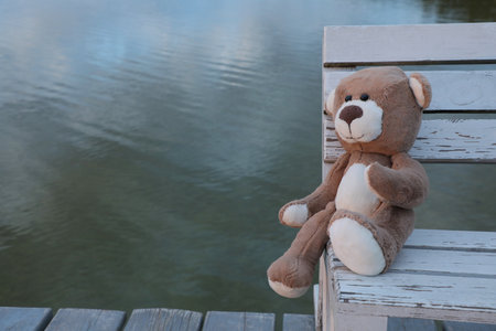 Lonely teddy bear on bench near river, space for textの写真素材