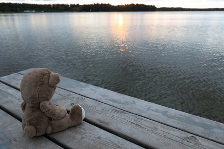 Lonely teddy bear on deck near river, space for textの写真素材