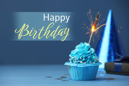 Happy Birthday greeting card. Sweet cupcake with sparkler on blue backgroundの写真素材