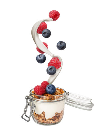 Fresh berries falling into jar cup with yogurt and granola on white background