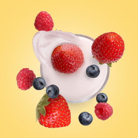 Fresh berries falling into glass of yogurt on golden background, top viewの写真素材