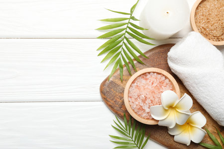 Spa composition with sea salt, plumeria flowers and burning candle on white wooden table, flat lay. Space for textの写真素材
