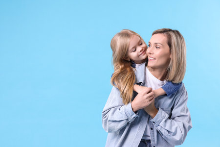 Cute little girl hugging her mom on light blue background, space for text. Happy Mother's Dayの写真素材