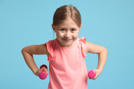 Cute little girl exercising with dumbbells on light blue backgroundの写真素材