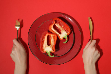Woman with cutlery and halves of bell pepper on red background, top viewの写真素材