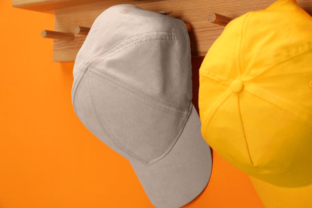 Stylish cap baseballs on orange wall, closeup. Mockup for design
