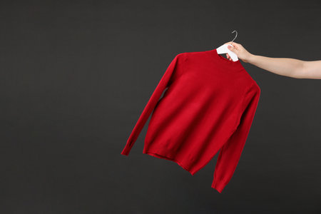 Woman holding hanger with red sweater on black background, closeup. Space for textの写真素材