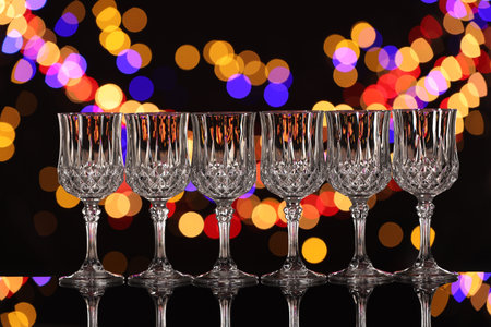 Empty wineglasses on mirror surface against black background with blurred lights, bokeh effectの写真素材