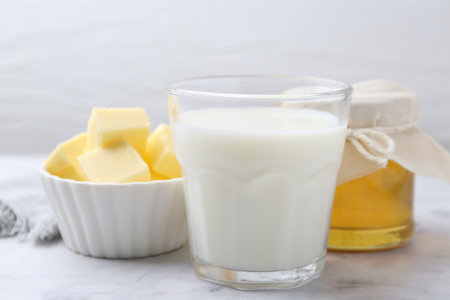 Fresh milk in glass, honey and butter on white marble table, closeupの写真素材