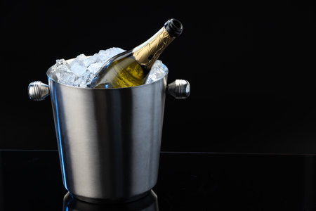 Bottle of sparkling wine in cooler bucket on black mirror surface. Space for textの写真素材