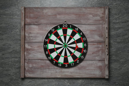 Dart board with colorful arrows and wooden planks hanging on grey wallの写真素材