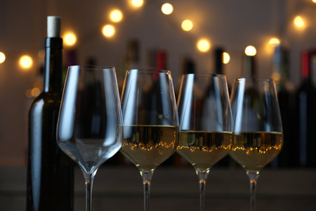 Tasty white wine in glasses against blurred background with festive lights, closeup. Bokeh effectの写真素材