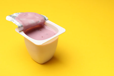 Delicious yogurt in plastic cup on yellow background, closeup. Space for textの写真素材