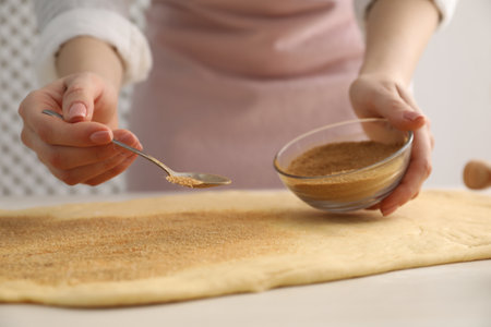 Making cinnamon rolls. Woman adding spice with sugar into dough at white wooden table, closeup