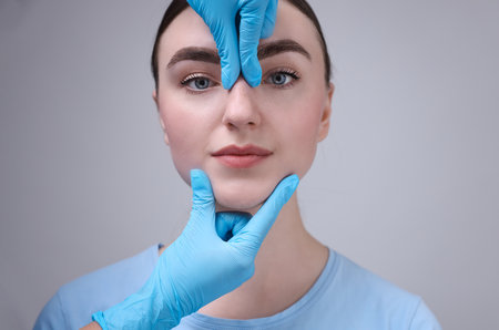 Doctor checking patient's nose before plastic surgery operation on grey background, closeupの写真素材