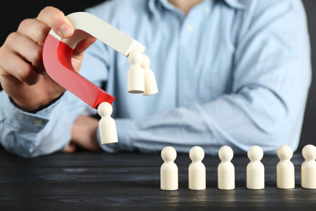 Man with magnet attracting human figures at black wooden table, closeupの写真素材