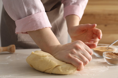 Woman kneading dough for cinnamon rolls at white wooden table, closeupの写真素材