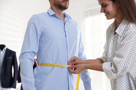 Woman measuring man's waist with tape in atelierの写真素材
