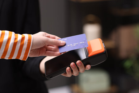 Woman paying with credit card via terminal against blurred background, closeup