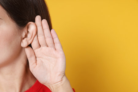 Woman showing hand to ear gesture on orange background, closeup. Space for text
