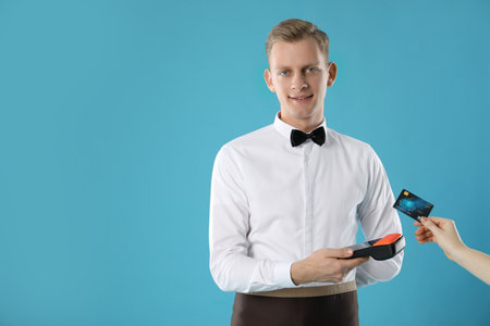 Waiter taking payment from client via terminal on light blue background, space for textの写真素材