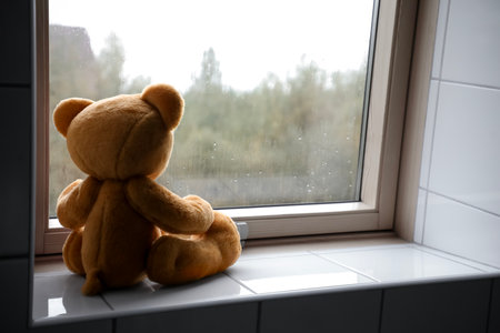 Lonely teddy bear near window on rainy day. Space for textの写真素材