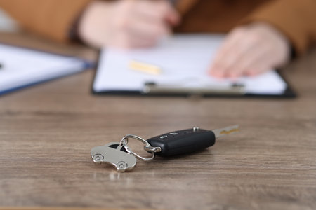 Car key and woman signing purchase agreement at wooden table, selective focus. Buying autoの写真素材