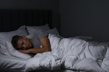 Young man sleeping in soft bed at nightの写真素材