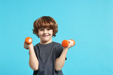 Little boy with dumbbells on light blue backgroundの写真素材