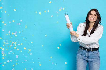 Happy woman blowing up confetti popper on light blue background, space for text. Surprise partyの写真素材