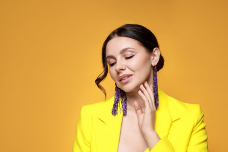 Beautiful young woman wearing stylish earrings on orange background. Space for textの写真素材
