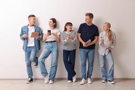 Group of people using different gadgets near white wall indoors. Modern technology