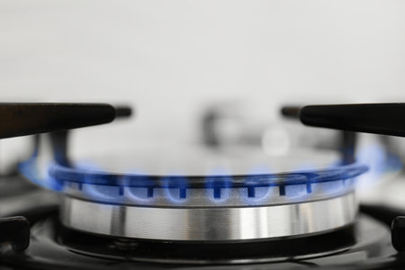 Gas burner of modern stove with burning blue flame, closeup