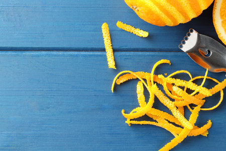 Fresh orange zest, fruits and zester on blue wooden table, flat lay. Space for textの写真素材