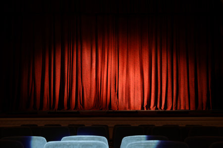 Elegant closed red curtains illuminated by spotlight in theaterの写真素材