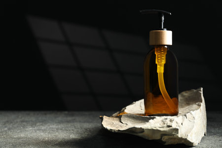 Bottle of cosmetic product and rock on gray table, space for textの写真素材