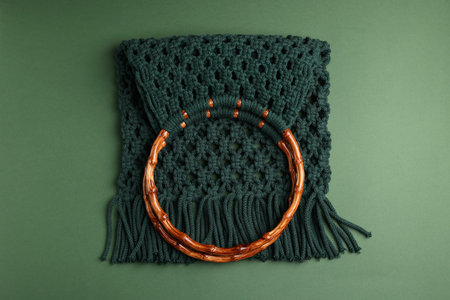 Macrame shopping bag with wooden handles on green background, top view
