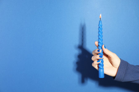 Woman holding burning candle on blue background, closeup. Space for textの写真素材