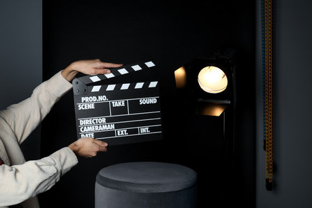 Woman with clapperboard near spotlight on black background, closeupの写真素材