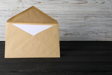 Kraft paper envelope with letter on black wooden table. Mockup for designの写真素材