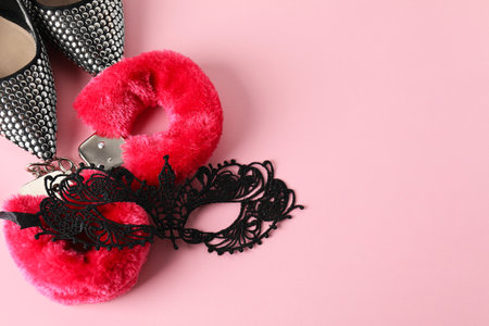 Fluffy handcuffs, lace mask and high-heeled shoes on pink background, flat lay. Space for textの写真素材