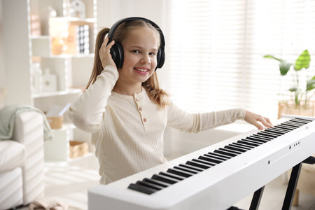Cute girl in headphones playing piano at homeの写真素材