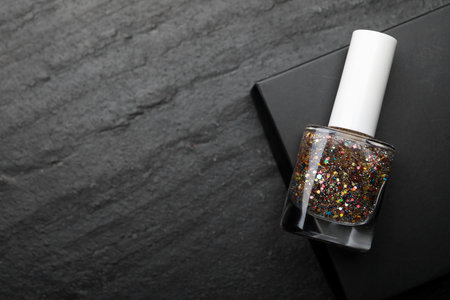 Glitter nail polish in bottle on dark textured table, top view. Space for textの写真素材