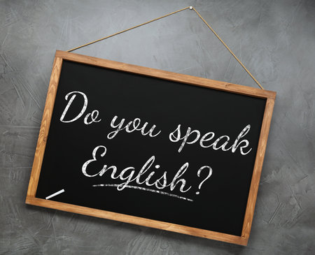 Small black chalkboard with text Do You Speak English? on gray background. Language courseの写真素材