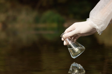 Examination of water quality. Researcher holding flask with sample from lake outdoors, closeup.