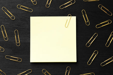 Paper notes and many golden clips on black wooden table, flat lay