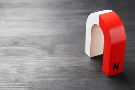 One horseshoe magnet on black wooden table, space for text