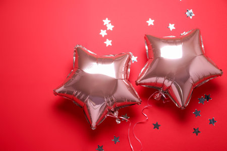 Star shaped pink balloons and confetti on red background, flat layの写真素材