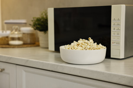 Bowl of popcorn near microwave oven on white marble countertop in kitchenの写真素材