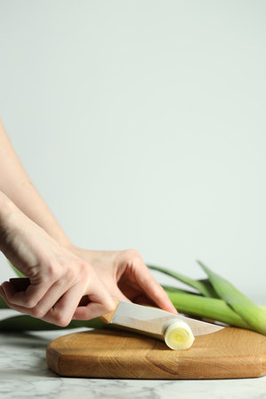 Woman cutting fresh leek at white table, closeup. Space for textの写真素材